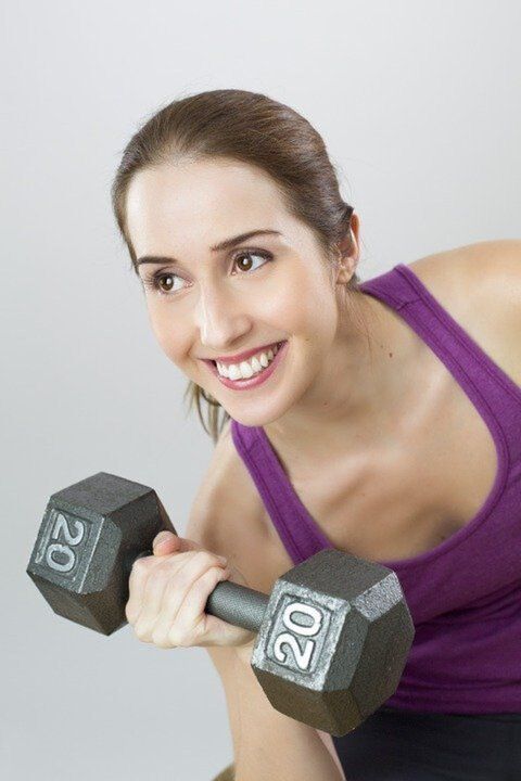 a girl with a dumbbell performs an exercise to lose weight